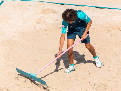 Ein Volunteer präpariert bei den Olympischen Spielen 2024 in Paris das Beachvolleyball-Feld