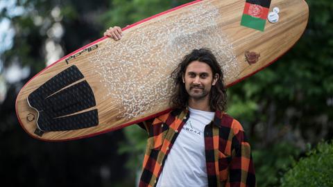 Afridun Amu mit Surfbrett, auf der eine Afghanistan-Flagge klebt.