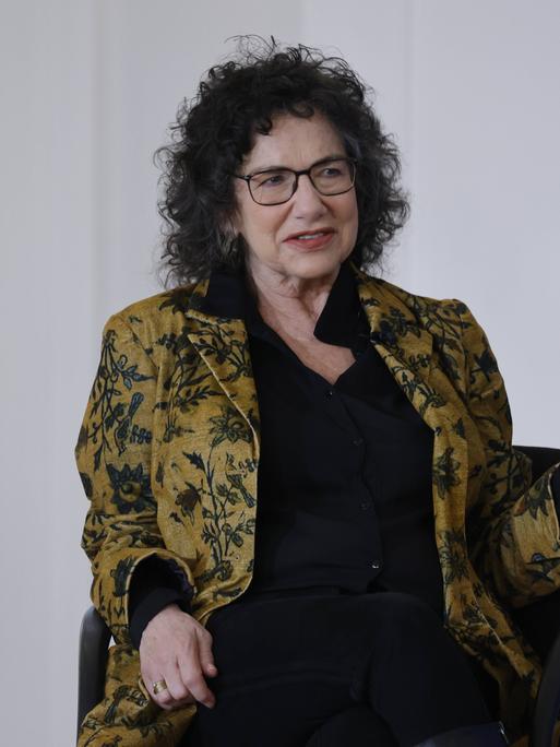 Susan Neiman sitzt in einer Gesprächssituation auf einem Sessel und hält mit der einen Hand einen Zeigefinger nach oben