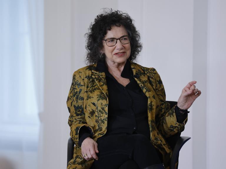 Susan Neiman sitzt in einer Gesprächssituation auf einem Sessel und hält mit der einen Hand einen Zeigefinger nach oben