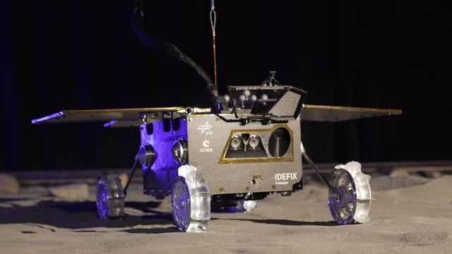 Das Bild zeigt eine Test-Version von dem Entdeckungs-Fahrzeug Idefix. Das Fahrzeug hat Räder und Sonnen-Panele. Es ist auf grauem Sand zu sehen.