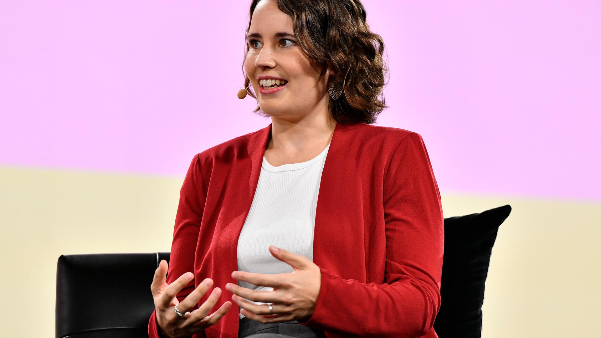 Helen Toner trägt eine schwarze Strickjacke und sitzt gestikulierend auf einer Bühne