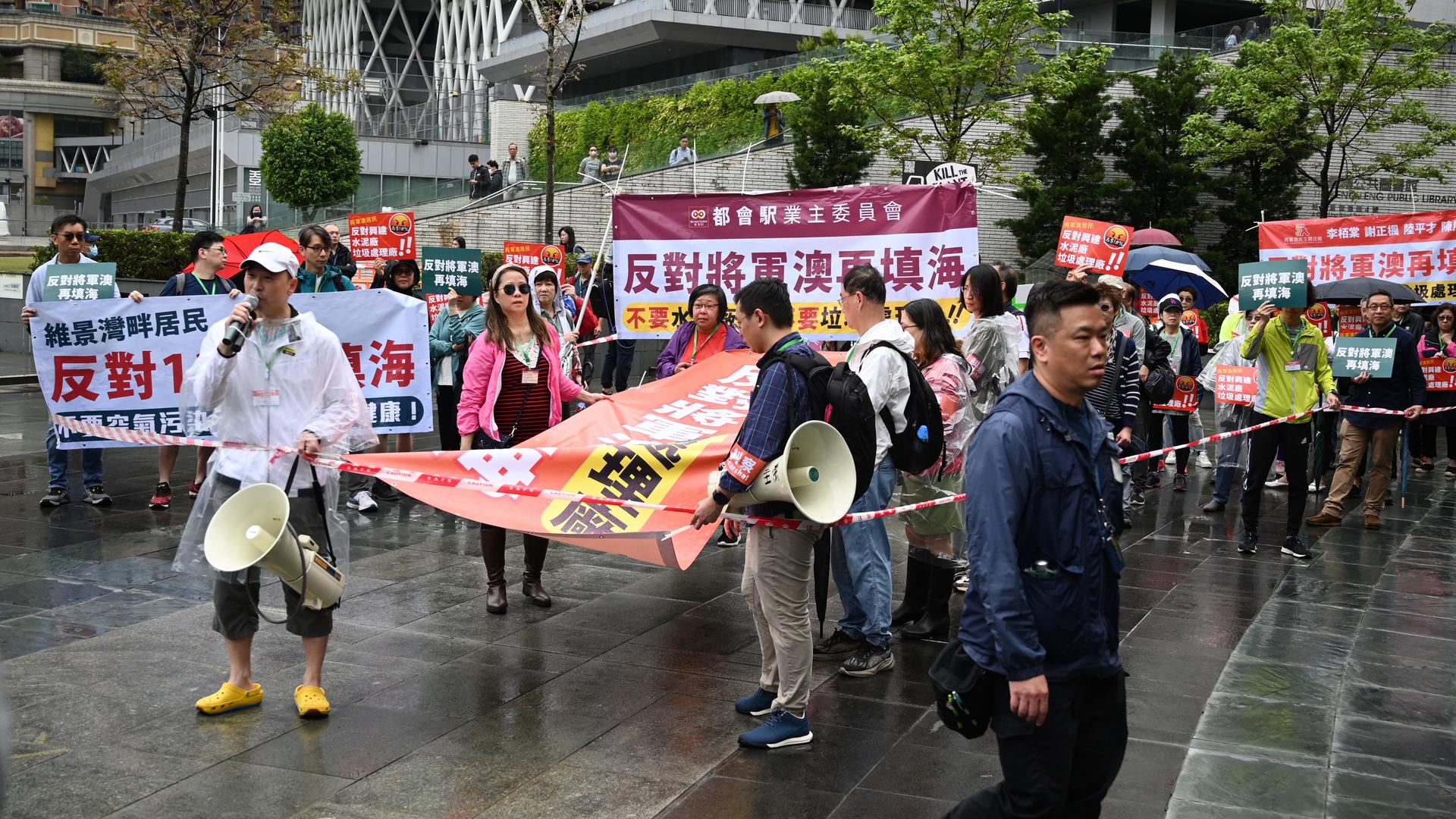 Eine Gruppe von Demonstranten hält Megafone und Plakate. Sie stehen auf der Straße hinter einem Absperrband.