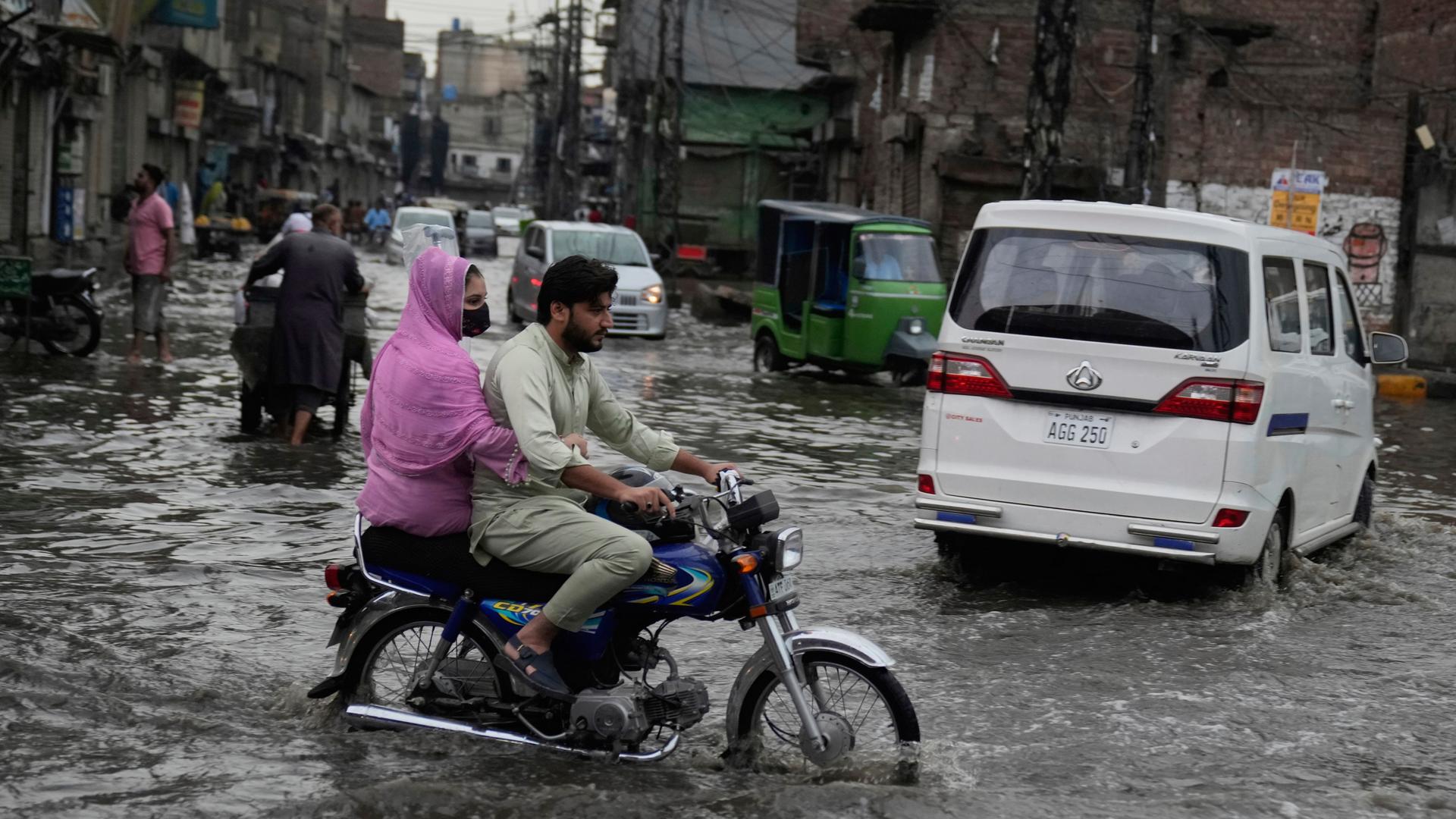 Menschen in Autos und Motorrädern fahren durch eine überschwemmte Straße in Lahore, Pakisten, die durch starken Monsunregen verursacht wurde.