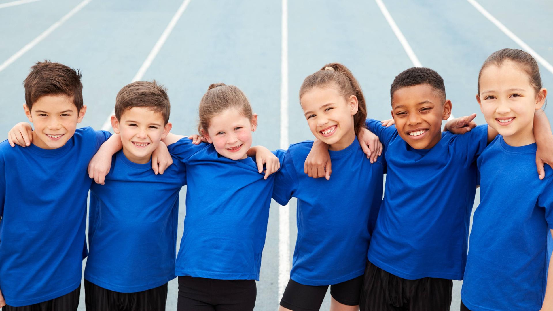 Das Foto zeigt Kinder in blauen Sport-Shirts. Sie umarmen sich und lächeln in die Kamera.