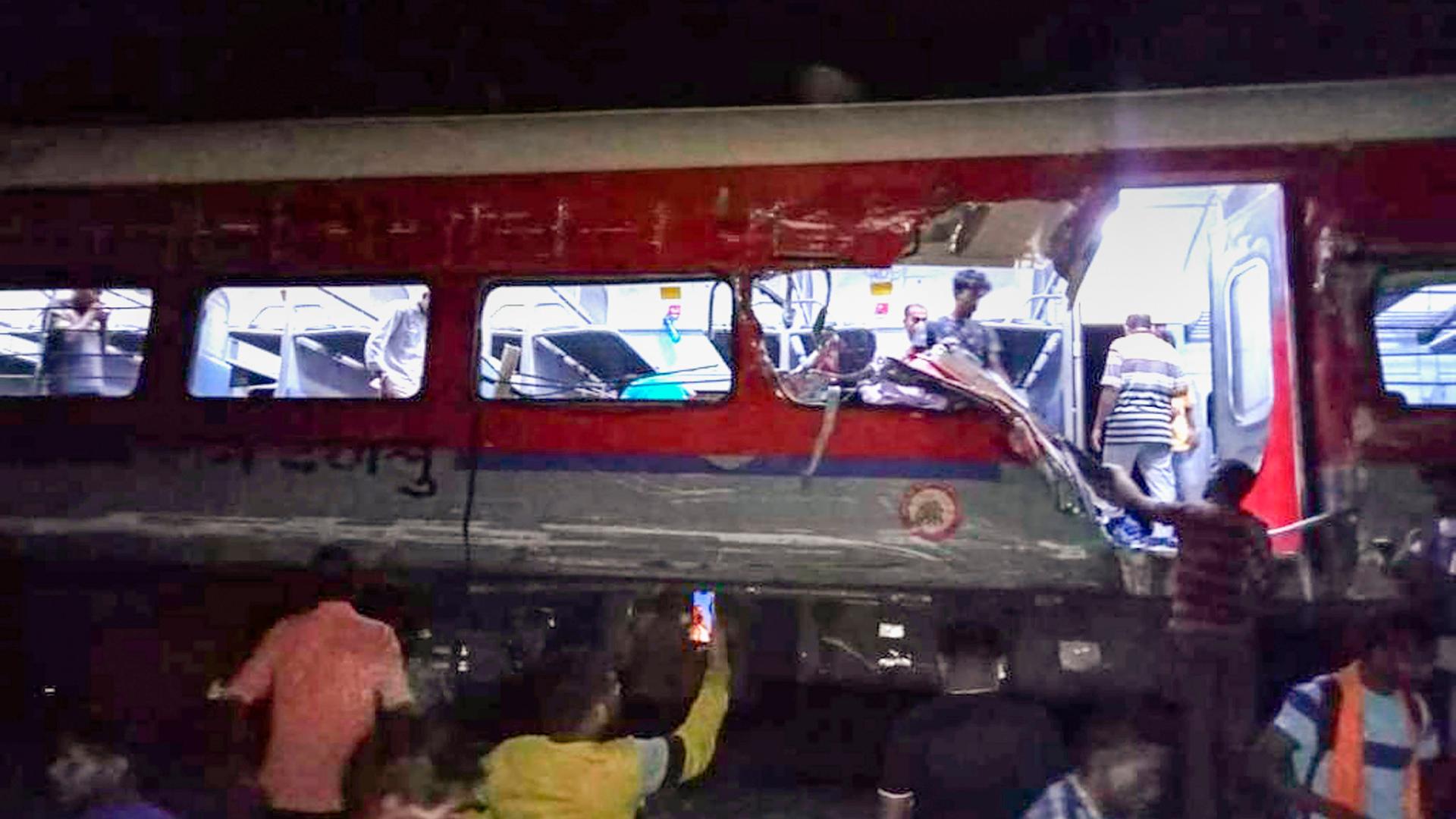 Mehrere Menschen stehen vor dem Waggon eines entgleisten Personenzugs in Indien, einige laufen innen durch das Abeteil. Mehrere Menschen stehen vor dem Waggon eines entgleisten Personenzugs in Indien, einige laufen innen durch das Abeteil.