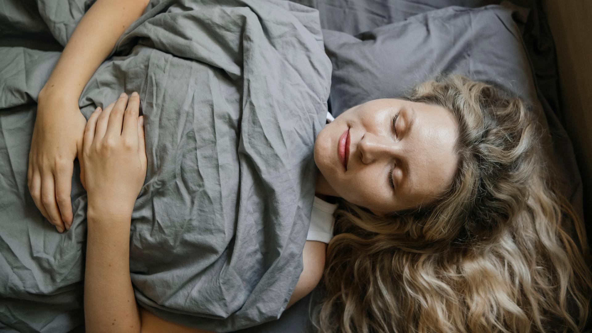EIne Frau liegt im Bett und hat ihre Augen geschlossen.