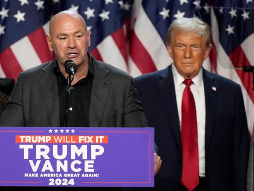 Dana White steht am Rednerpult. Donald Trump steht versetzt dahinter und hört zu.