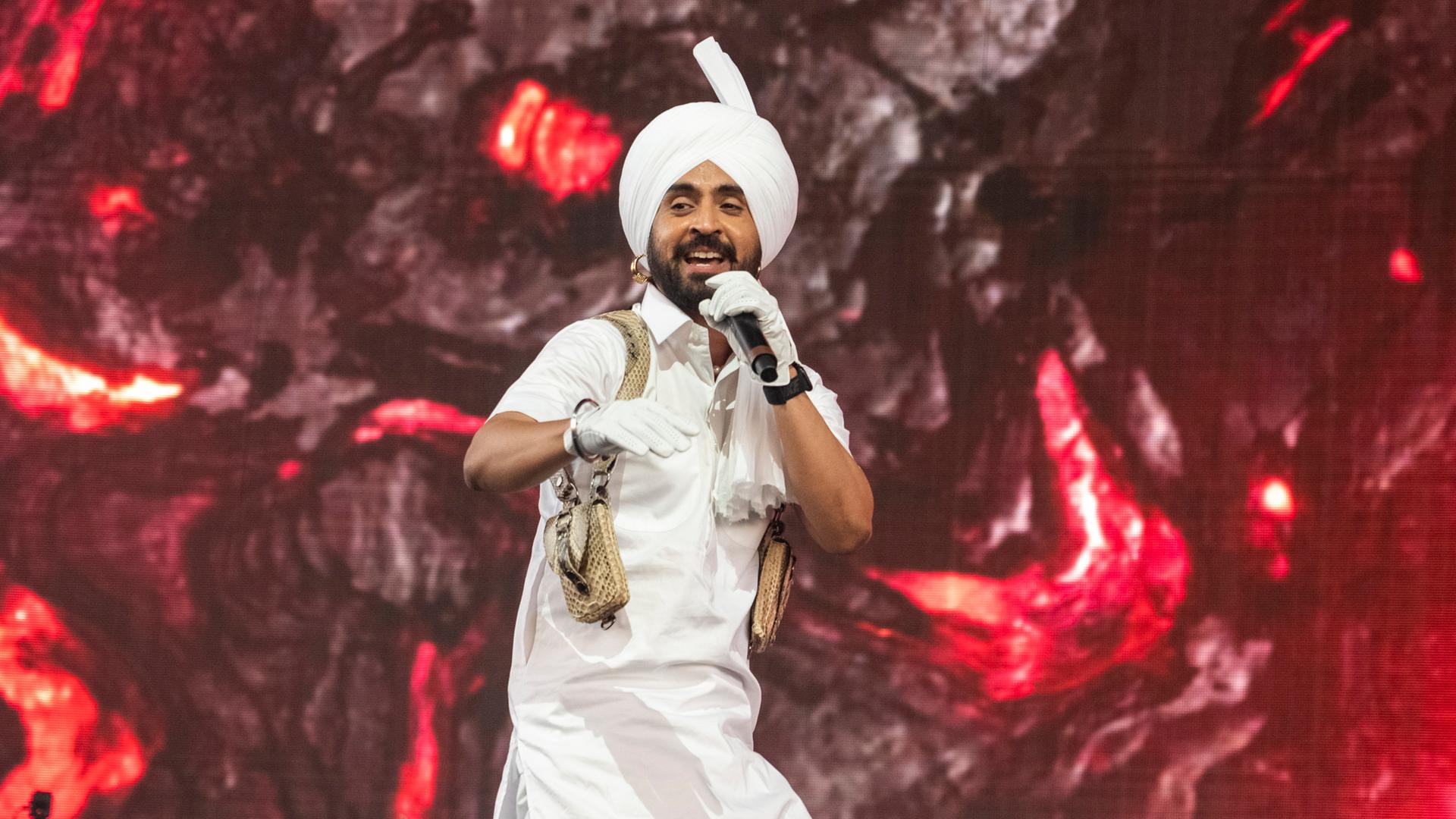 Diljit Dosanjh mit Turban im traditionellen weißen Gewand auf der Bühne Diljit Dosanjh mit Turban im traditionellen weißen Gewand auf der Bühne