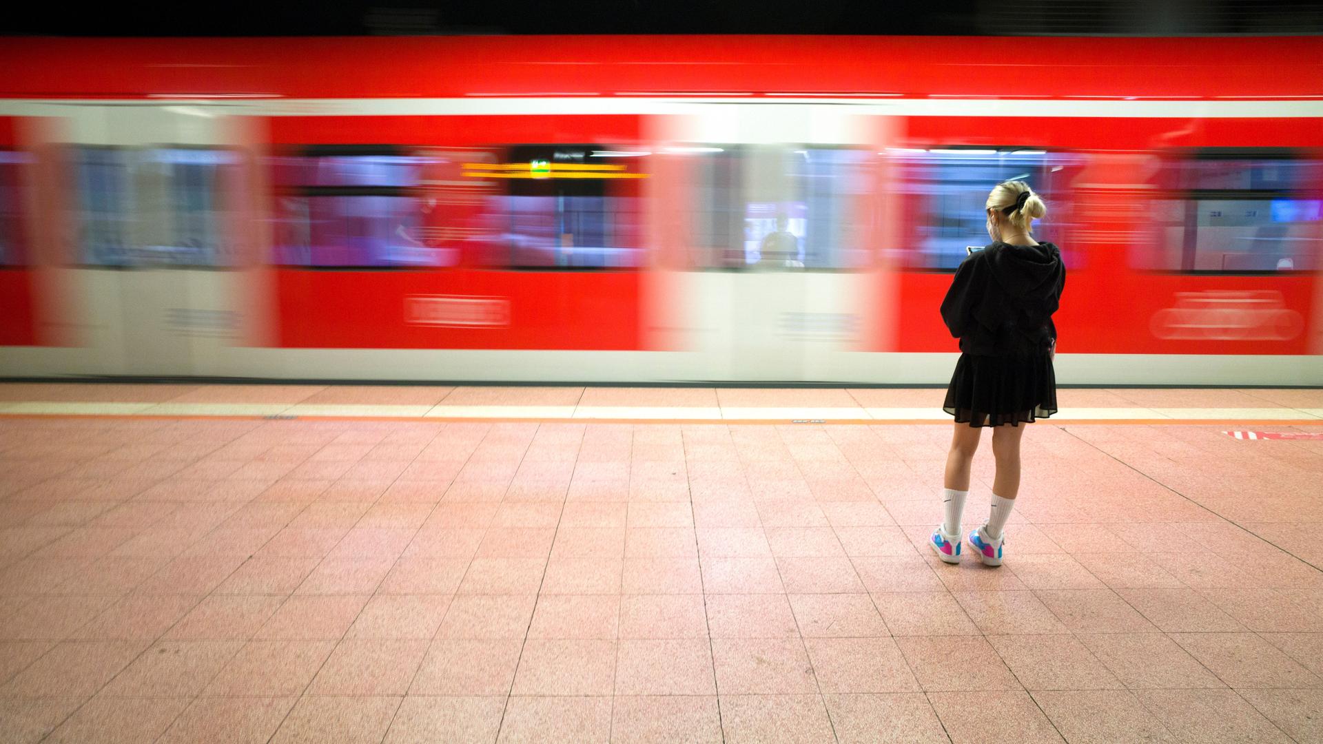 Eine junge Frau steht an einem Bahngleis, ein Zug fährt vorbei.
