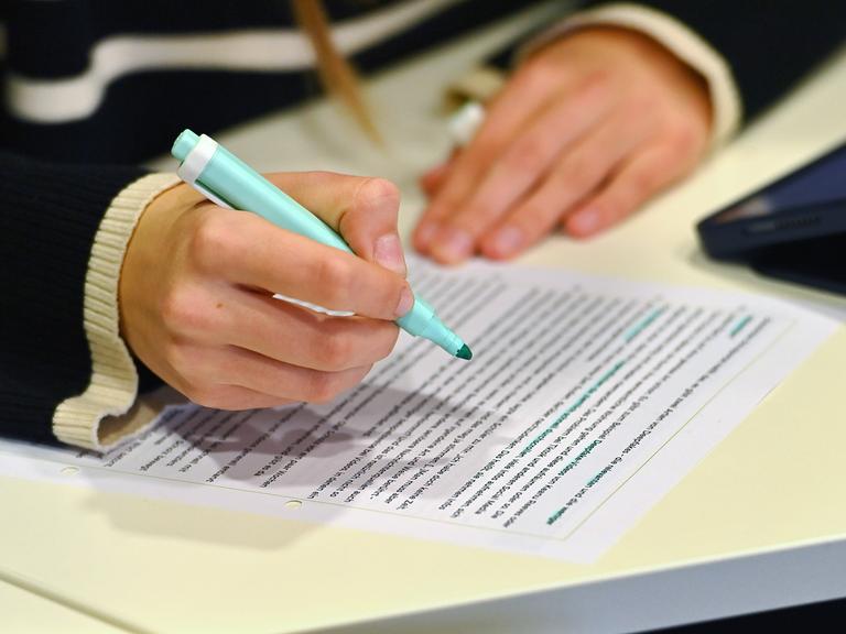 Hände einer Schülerin mit Textmarker und Arbeitsblatt