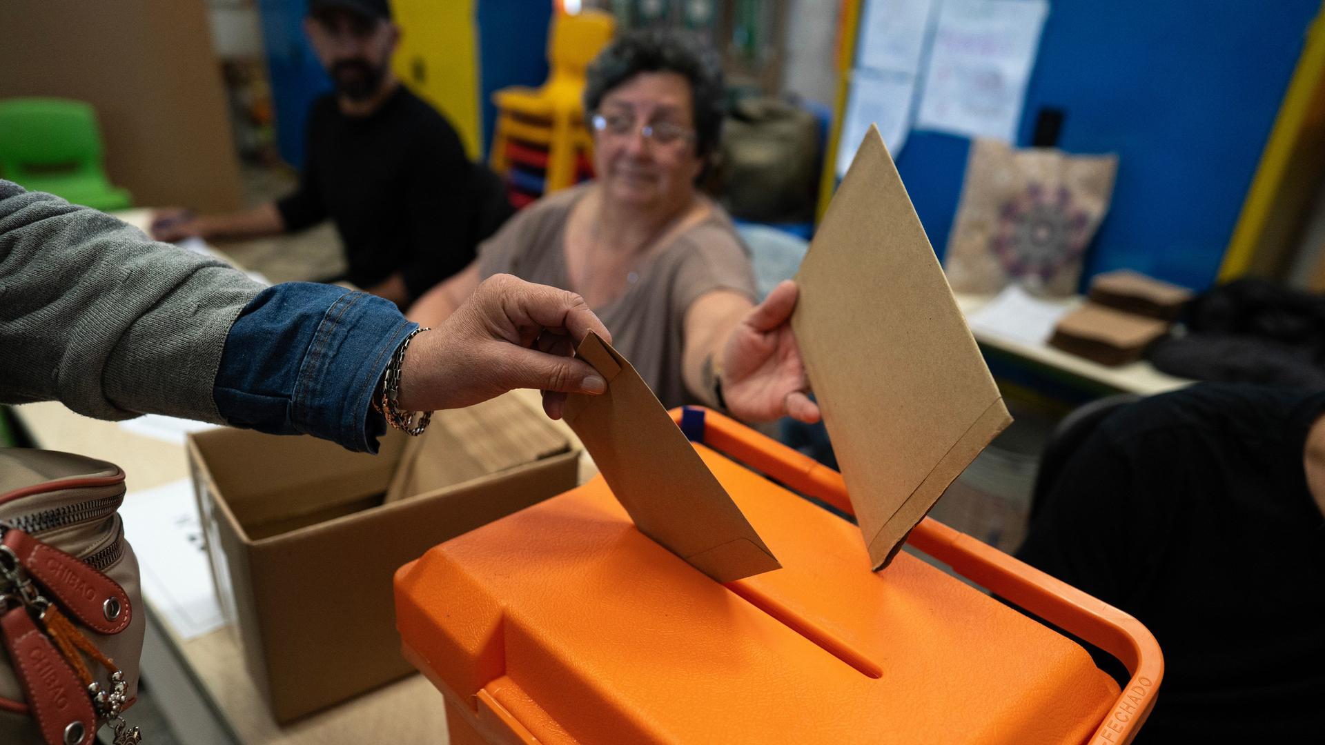 Das Bild zeigt zwei Hände mit Stimmzetteln über einer Wahlurne in einem Wahllokal in Montevideo. 