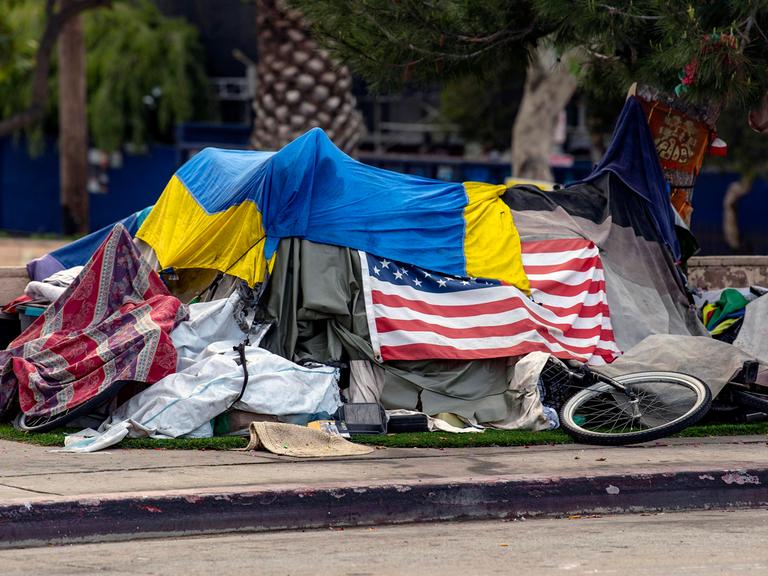Das Zelt eines Obdachlosen am Straßenrand ist mit der amerikanischen und der ukrainischen Flagge bedeckt.
