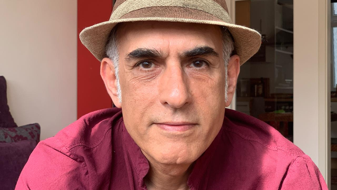 Der iranische Autor Bahram Moradi lächelt in die Kamera. Er trägt ein rotes Hemd und einen braunen Hut.