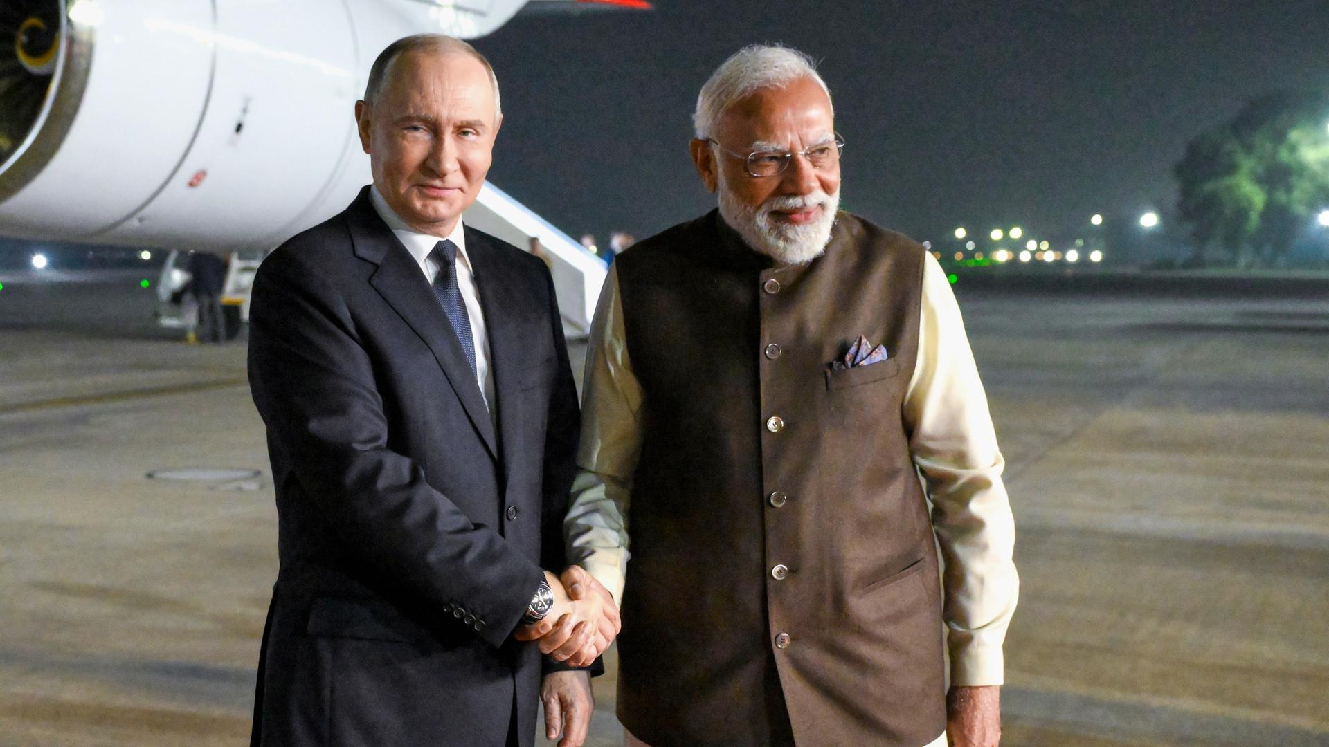 Der russische Staatschef Putin und Indiens Premier Modi schütteln sich am Flughafen die Hand. Im Hintergrund ist ein Flugzeug.