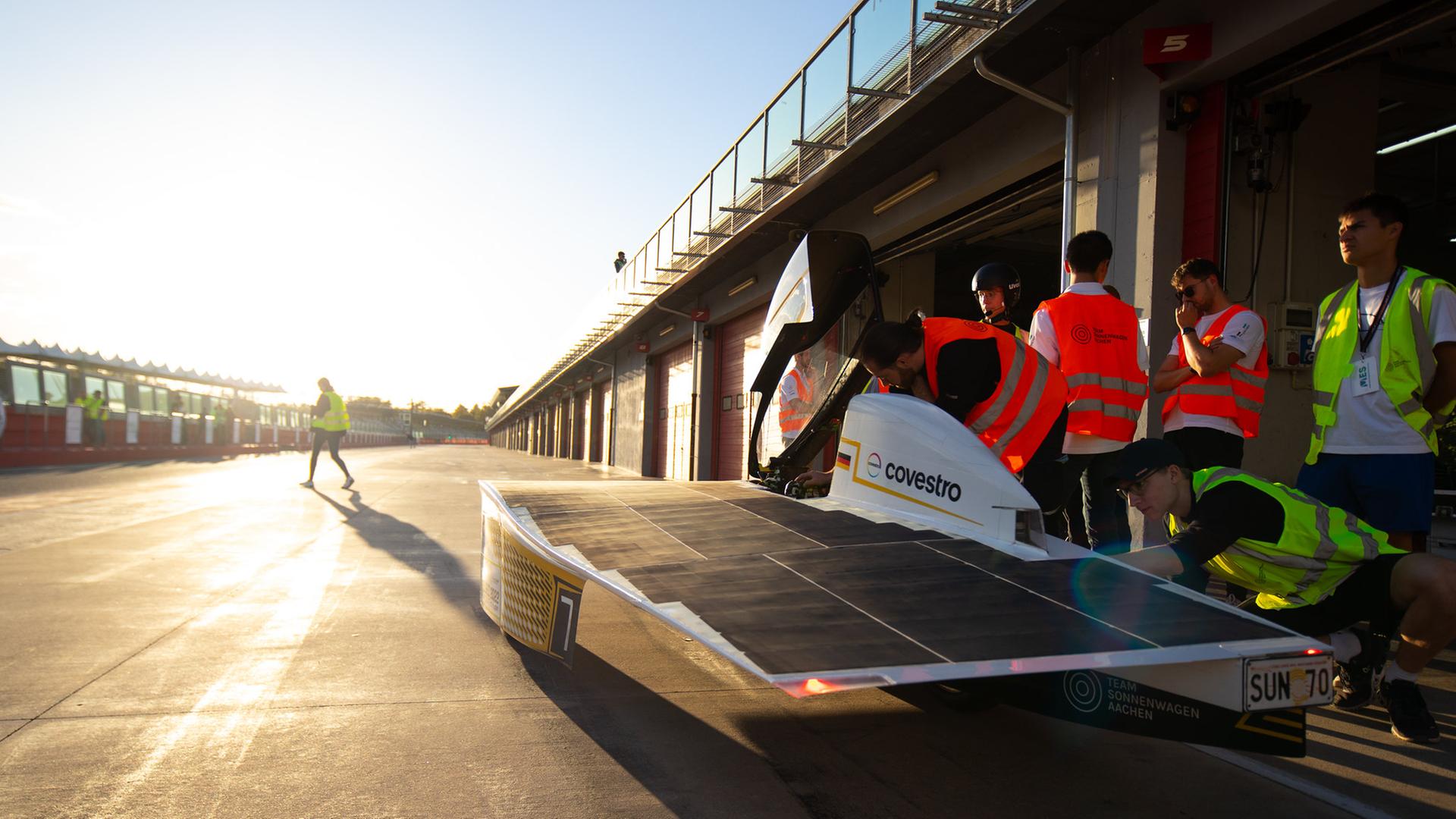 Das Vorläufer-Sonnenmobil des Aachener Teams Sonnenwagen bei einem Rennen. Zu sehen ist das windschnittige Mobil auf einer Rennstrecke, im Hintergrund die Sonne im Dämmerlicht. 