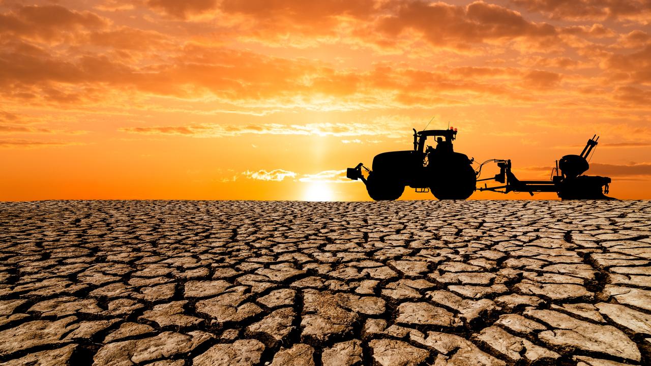 Auf einem völlig ausgetrockneten erdboden ist ein Traktor mit landwirtschaftlichem Anhänger vor untergehender Sonne zu erkennen.