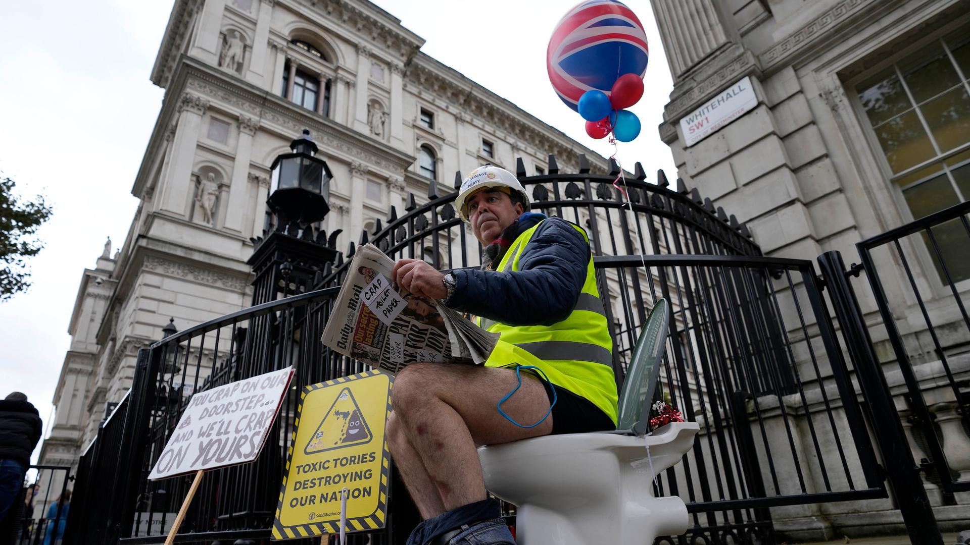 Ein Mann sitzt in London auf einer Toilette, die vor dem Cabinets Office steht, und liest Zeitung bei einem Protest gegen die Ableitung von nicht vollständig gereinigtem Wasser in Flüsse und ins Meer.