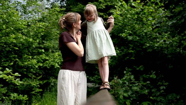 Eine Frau hält ihre Tochter, die auf einem Stamm balanciert. Beide lachen.