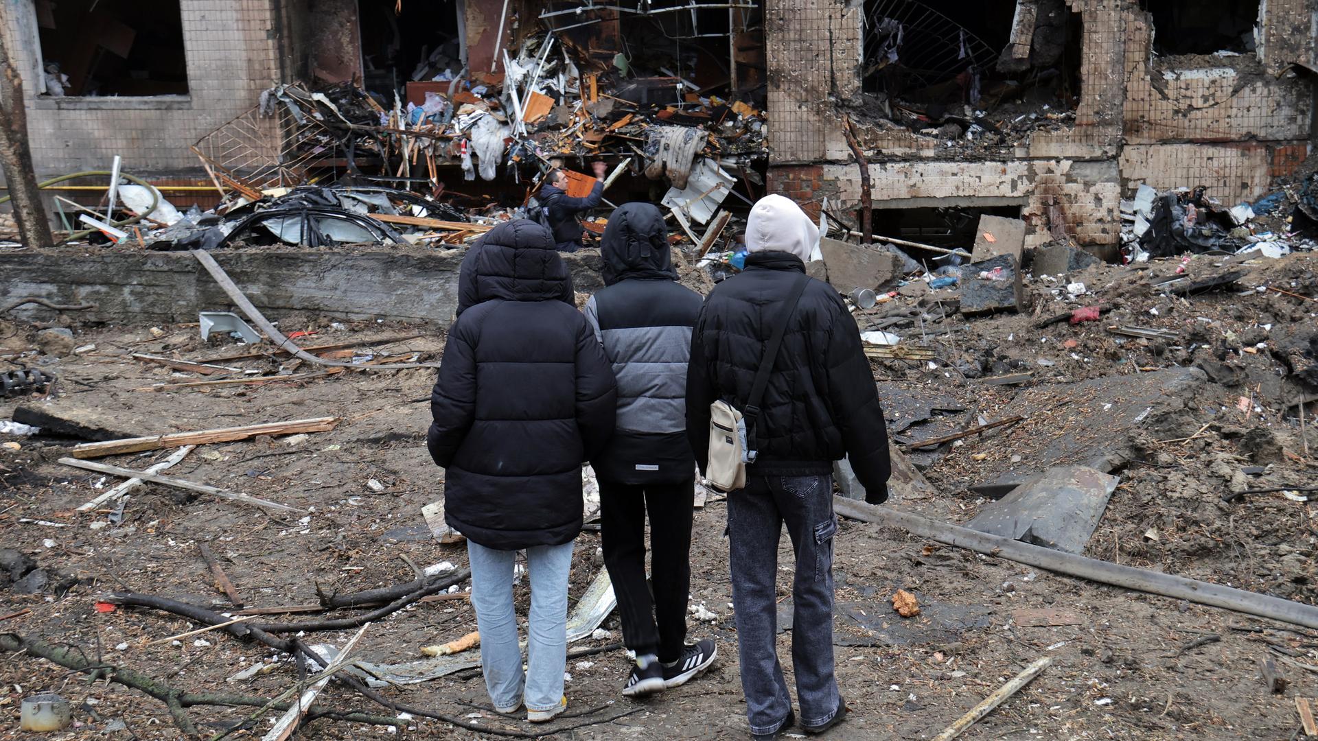 Drei Jugendliche betrachten in der Hauptstadt Kiew die Zerstörungen, die durch herabfallende Raketentrümmer in einem Wohnhaus im Solomianskyi-Viertel verursacht wurden, das bei dem groß angelegten russischen Raketenangriff beschädigt wurde.