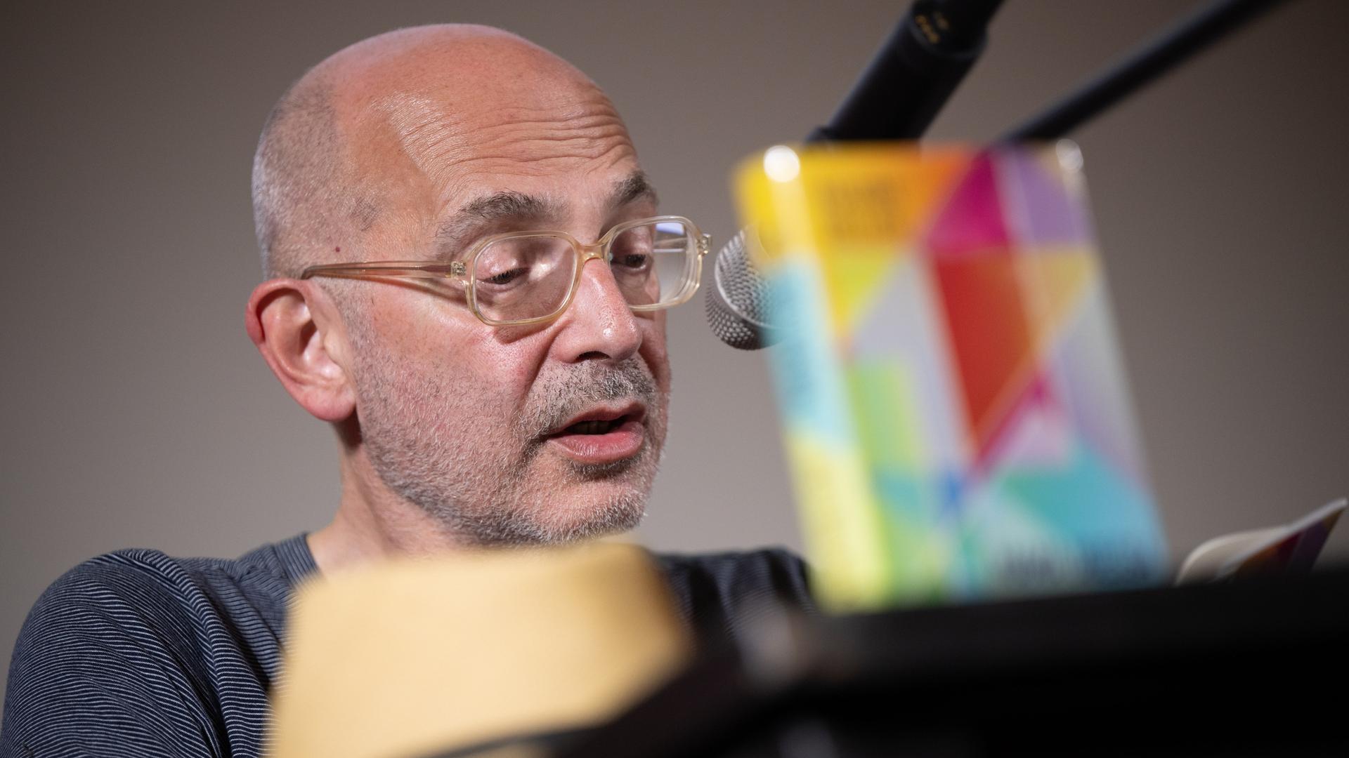 Der Schriftsteller Maxim Billder sitzt auf einer Bühne, trägt Brille und spricht ins Mikrofon