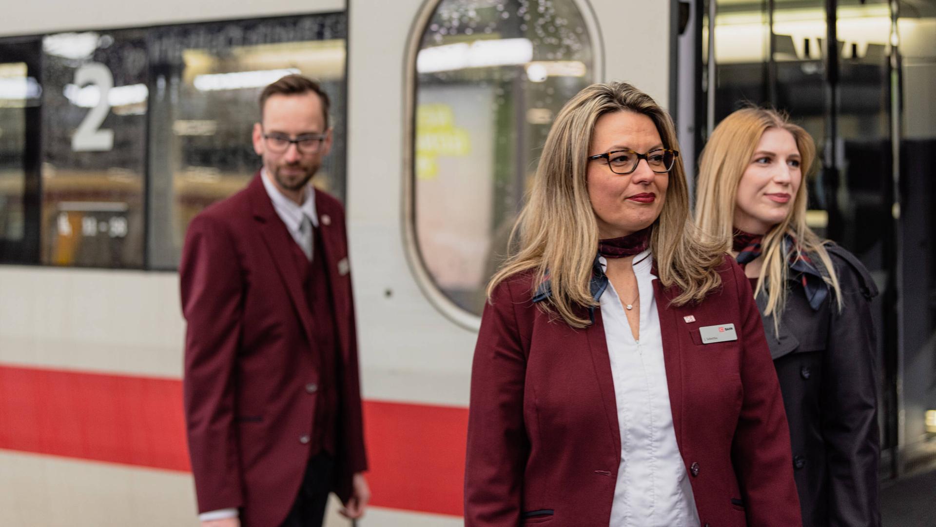 Drei Beschäftigte der Deutschen Bahn, ein Mann und zwei Frauen, stehen vor einem ICE.