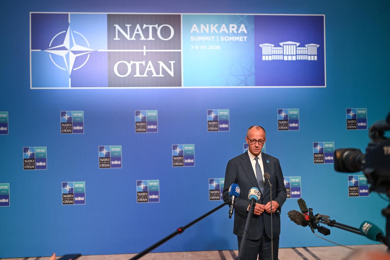 Bundeskanzler Merz steht beim NATO-Gipfel in Ankara vor einer Wand, auf der das NATO-Logo zu sehen ist. Auf Merz sind mehrere Mikrofone und eine Kamera gerichtet.