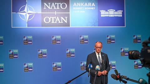 Bundeskanzler Merz steht beim NATO-Gipfel in Ankara vor einer Wand, auf der das NATO-Logo zu sehen ist. Auf Merz sind mehrere Mikrofone und eine Kamera gerichtet.