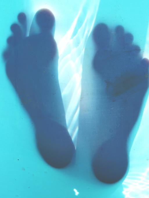 Transparente Unterseite eines Wasserbeckens, auf der sich die Silhouetten zweier Füße abzeichnen.