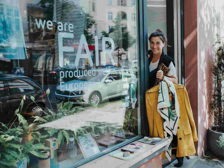 Die Stylistin Janine Dudenhöffer steht im Eingang eines Modegeschäfts, sie hält einen gelben Mantel auf einem Kleiderbügel in der Hand.