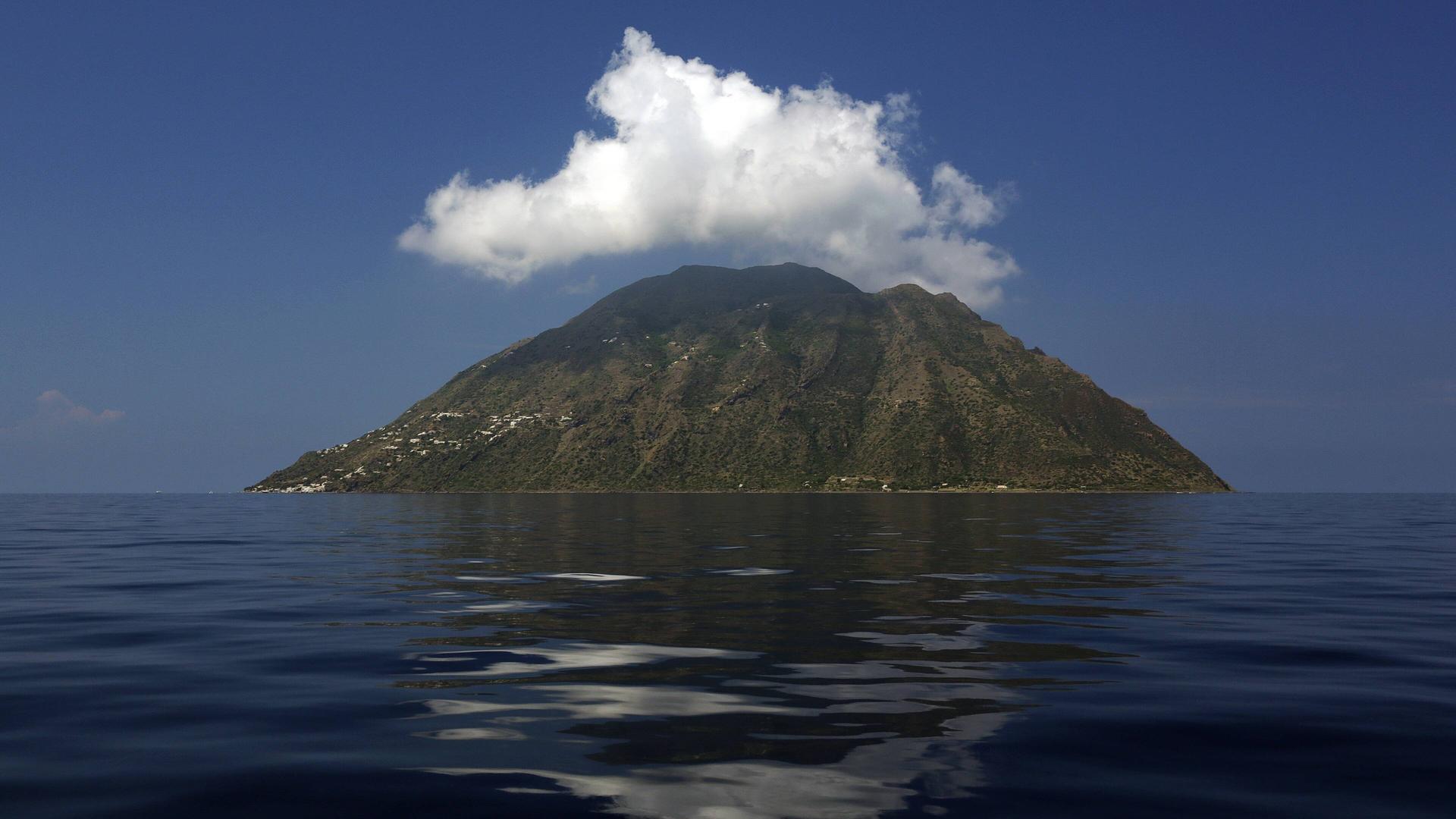 Blick auf die Insel Alicudi im Meer über der eine weiße Wolke schwebt