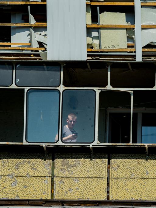 Ein Mann blickt aus einem zerstörten mehrstöckigen Haus durch ein Fenster.