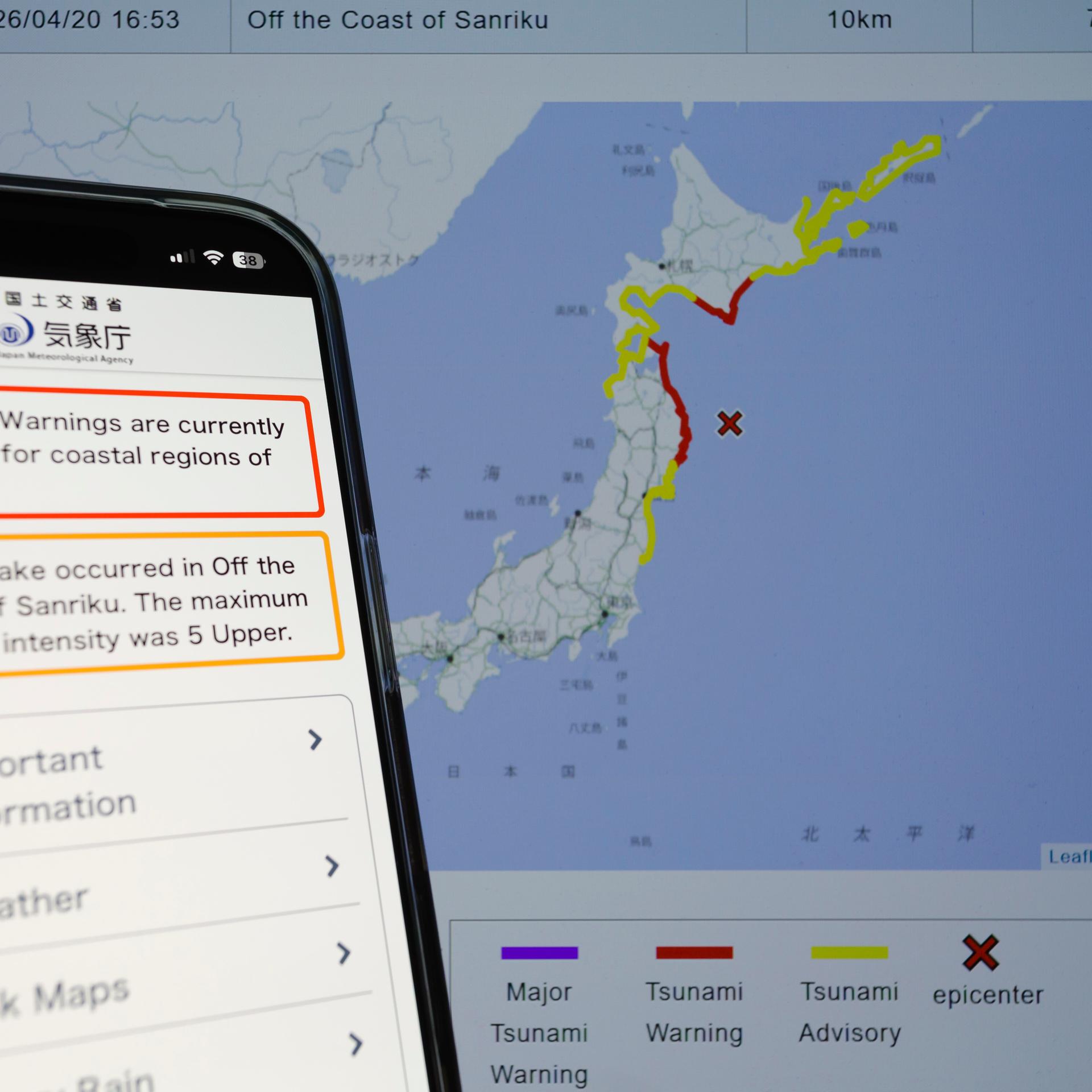 Auf einem Smartphone ist mit einer von der Behörde herausgegebenen Tsunamiwarnungskarte im Hintergrund zu sehen.