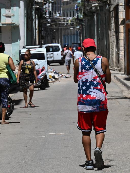 Ein Mann in einem T-Shirt mit der US-Flagge geht durch eine Straße in Havanna. Er ist von hinten nicht zu erkennen.