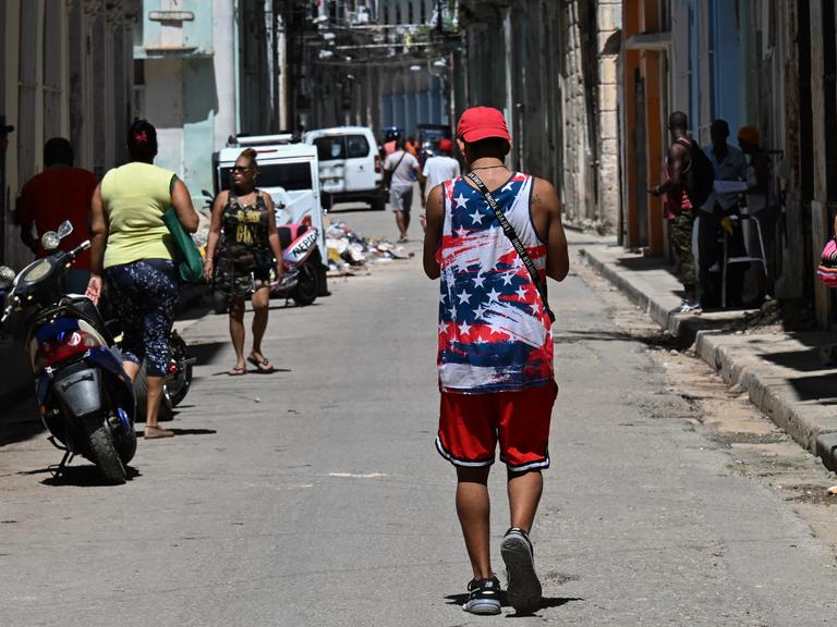 Ein Mann in einem T-Shirt mit der US-Flagge geht durch eine Straße in Havanna. Er ist von hinten nicht zu erkennen.