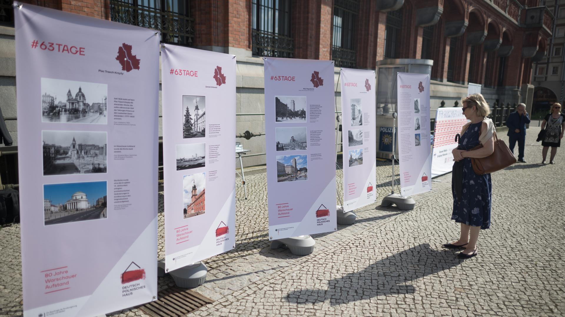 Eine Frau schaut sich vor einer Gedenkveranstaltung zu 80 Jahre Warschauer Aufstand des Deutsch-Polnischen Hauses und des Landes Berlin am Roten Rathaus Plakatwände an.