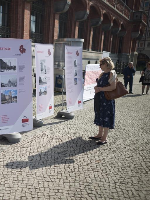 Eine Frau schaut sich vor einer Gedenkveranstaltung zu 80 Jahre Warschauer Aufstand des Deutsch-Polnischen Hauses und des Landes Berlin am Roten Rathaus Plakatwände an.