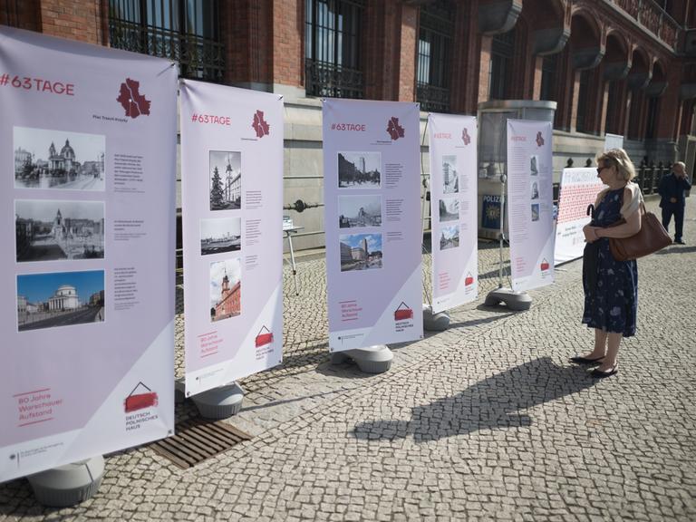 Eine Frau schaut sich vor einer Gedenkveranstaltung zu 80 Jahre Warschauer Aufstand des Deutsch-Polnischen Hauses und des Landes Berlin am Roten Rathaus Plakatwände an.