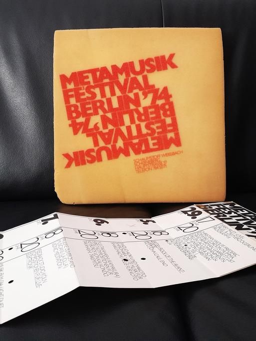 Ein mit roten Buchstaben bedrucktes Sitzkissen und ein entfalteter Flyer liegen auf einem schwarzen Ledersitz