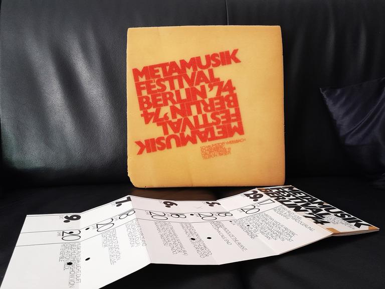Ein mit roten Buchstaben bedrucktes Sitzkissen und ein entfalteter Flyer liegen auf einem schwarzen Ledersitz