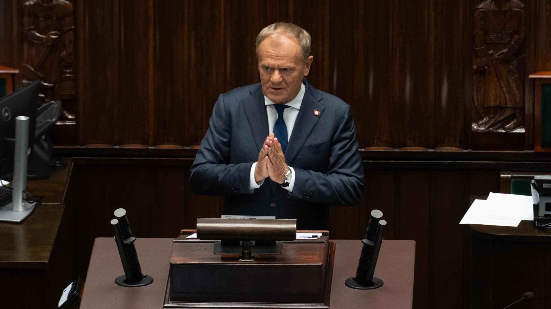 Ministerpräsident Donald Tusk bittet bei seiner Rede im polnischen Parlament um Zustimmung für seinen pro-europäischen Reformkurs. Er schaut eindringlich und hat die Hände gefaltet, als würde er an die Zuhörer appellieren. 