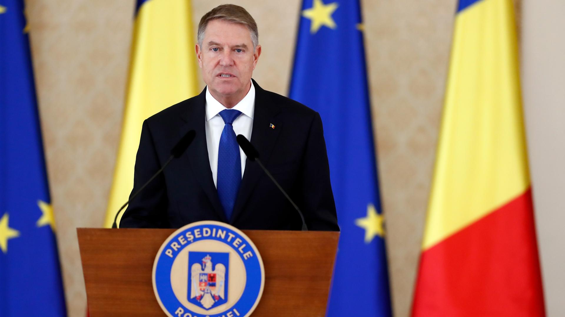 Rumäniens Präsident Iohannis spricht an einem Rednerpult. Hinter ihm sind rumänische und europäische Flaggen. 