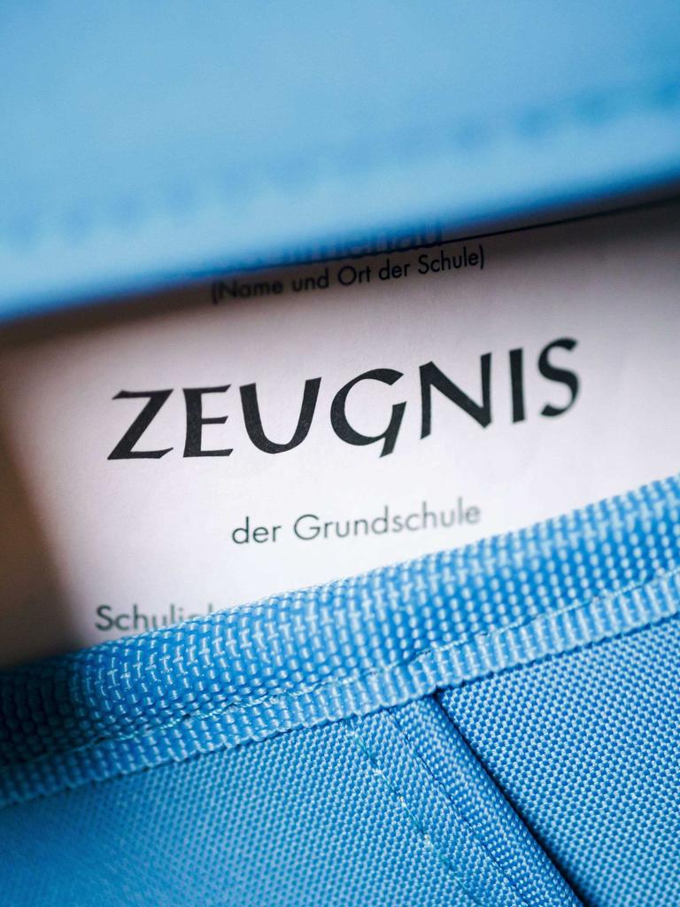 Nahaufnahme eines blauen Schulranzens, aus dem ein Zeugnis guckt.
