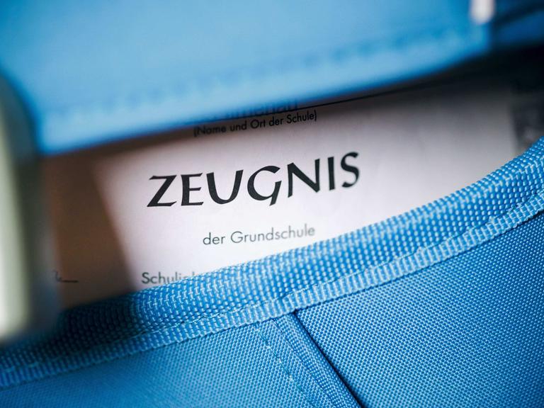 Nahaufnahme eines blauen Schulranzens, aus dem ein Zeugnis guckt.