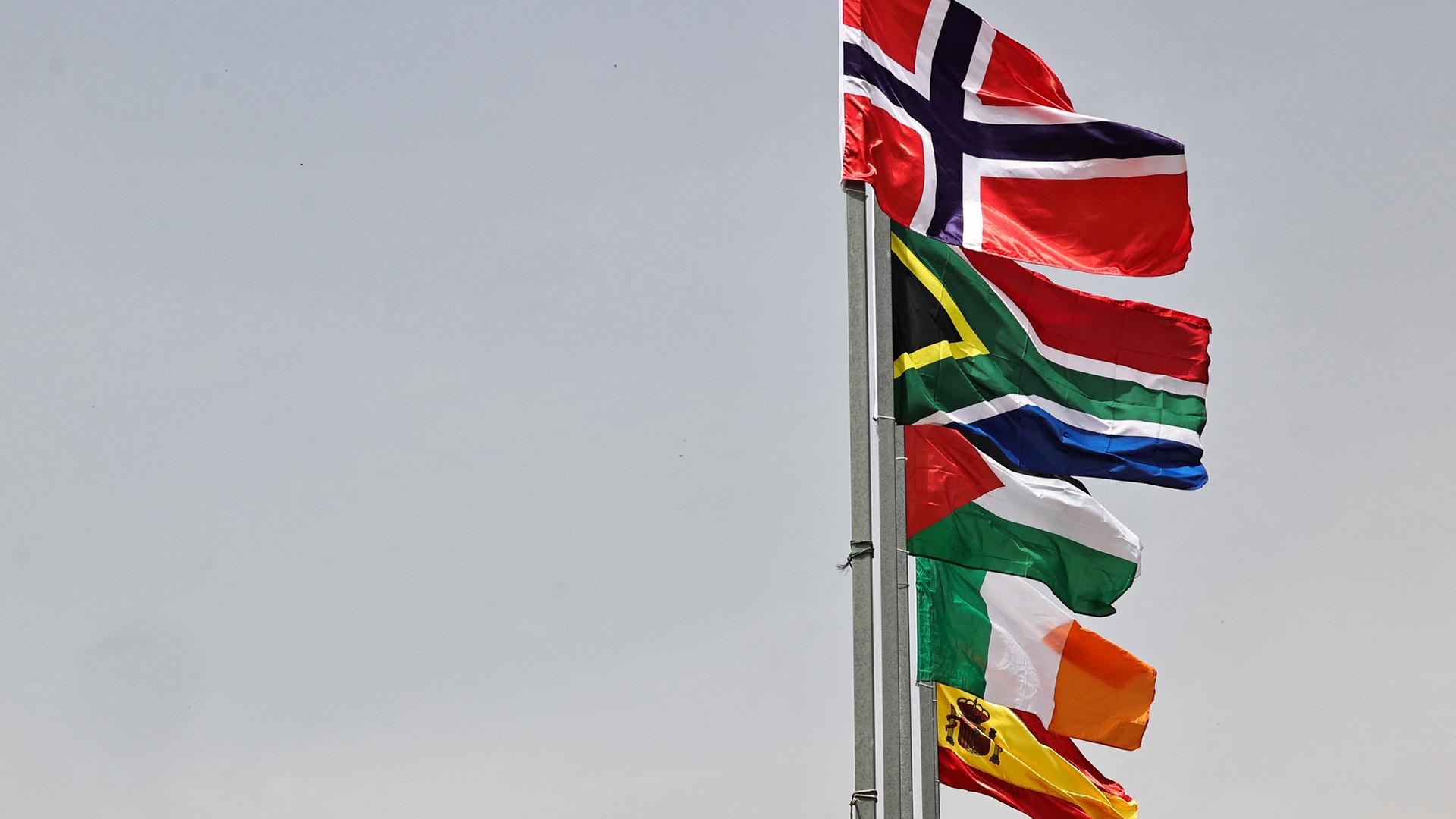 Die Fahnen von Norwegen, Südafrika, Palästina, Irland und Spanien hängen untereinander an einem Mast und wehen im Wind.