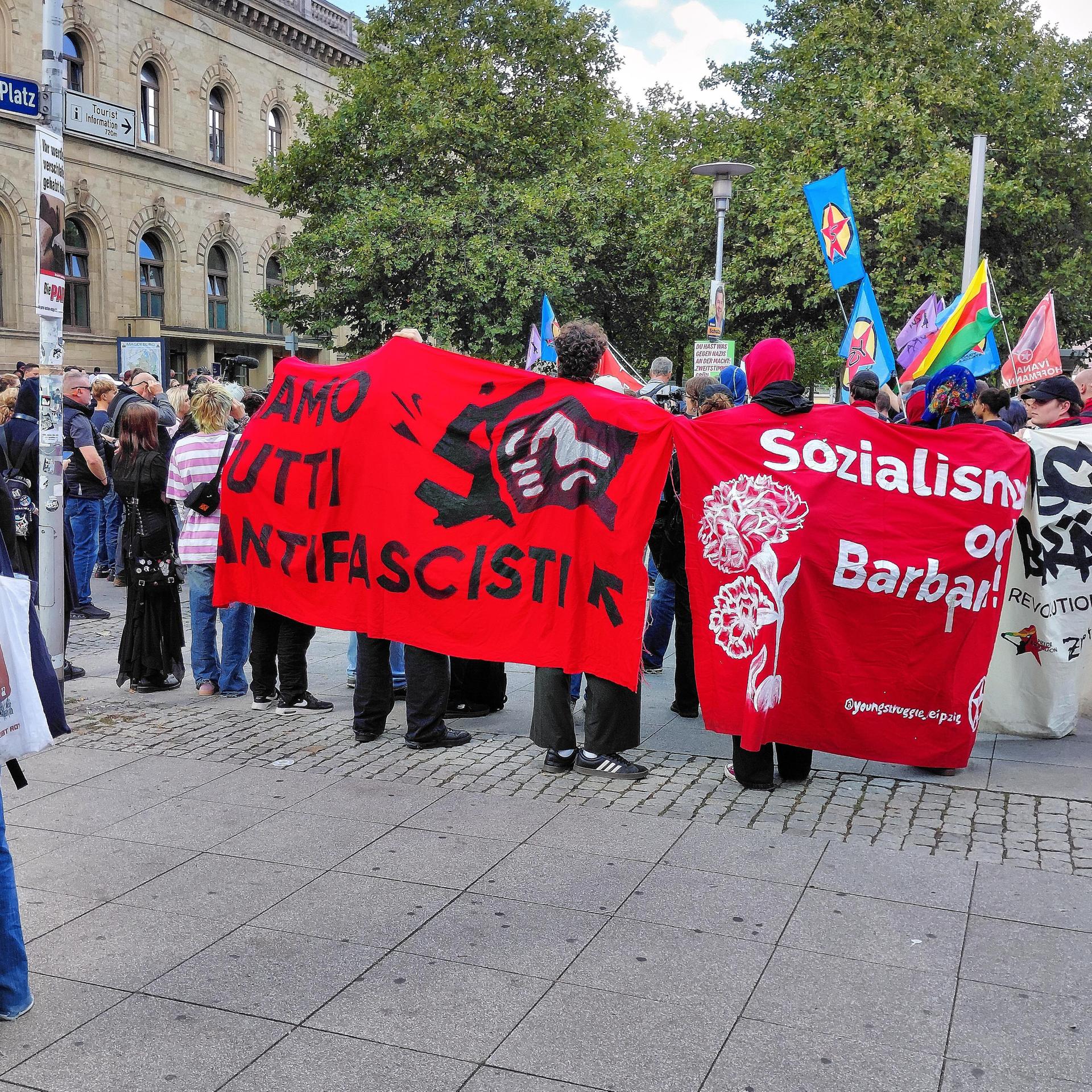 Dutzende Demonstranten haben sich vor dem Hauptbahnhof in Magdeburg versammelt. Viele tragen Banner aus dem linksextremen Milieu.