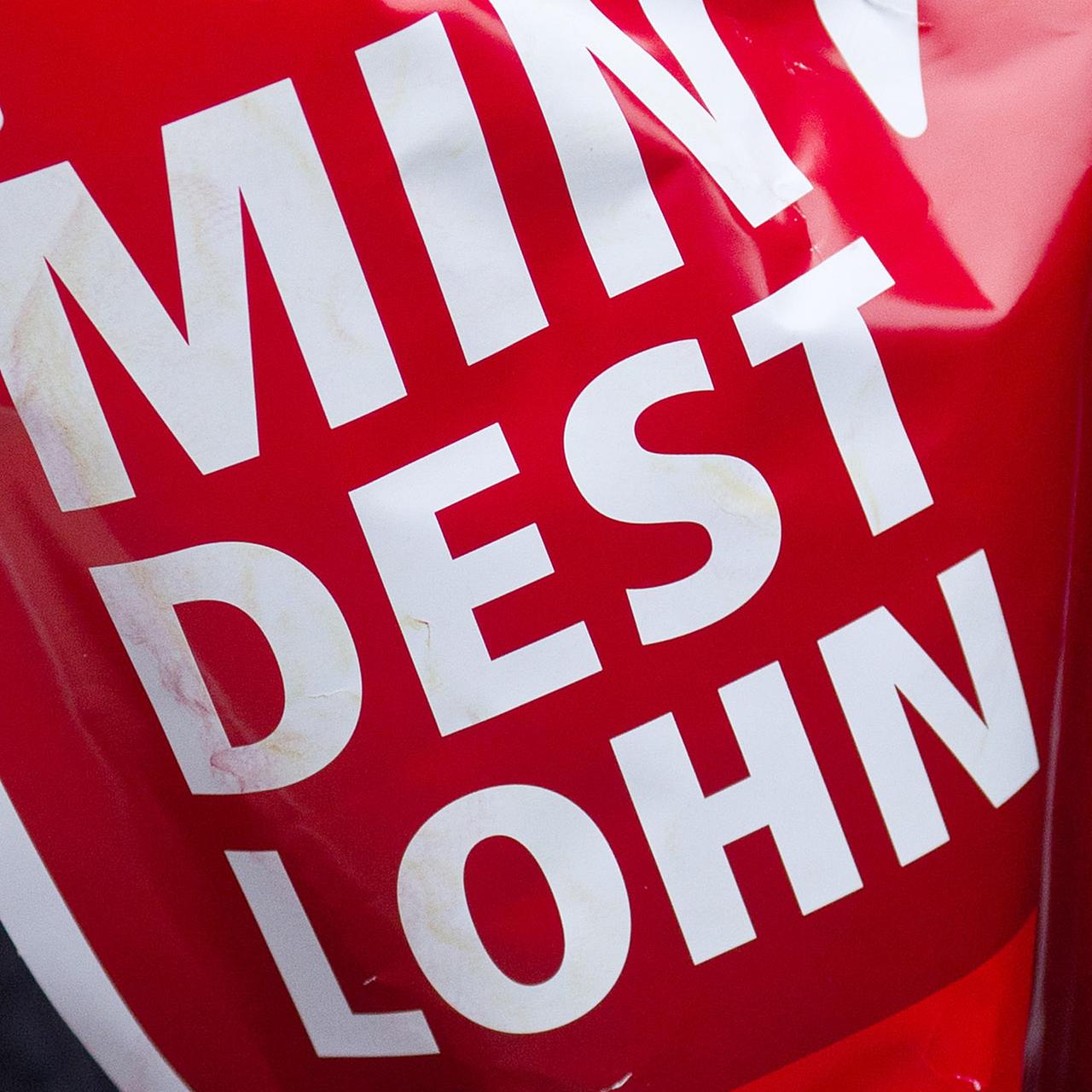 Ein rotes Schild mit der Aufschrift "Mindestlohn" wird während einer Aktion des Deutschen Gewerkschaftsbundes (DGB) hochgehalten.