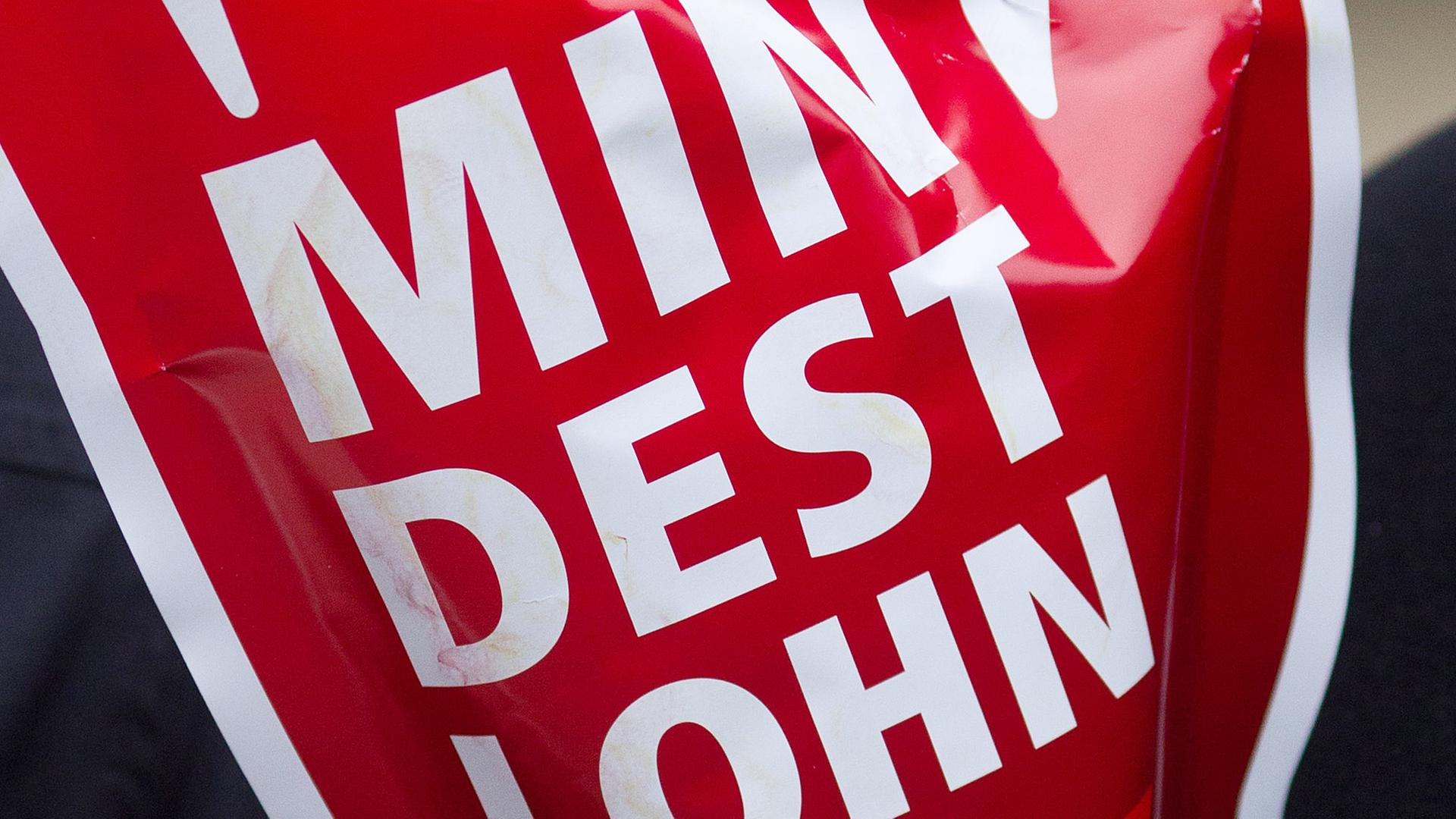 Ein rotes Schild mit der Aufschrift "Mindestlohn" wird während einer Aktion des Deutschen Gewerkschaftsbundes (DGB) hochgehalten.