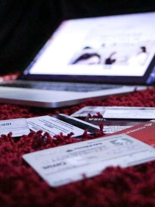 Ein Laptop steht geöffnet auf einem roten Teppich. Davor liegen viele Chipkarten.