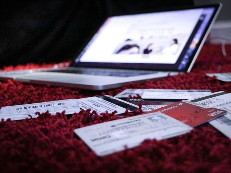 Ein Laptop steht geöffnet auf einem roten Teppich. Davor liegen viele Chipkarten.